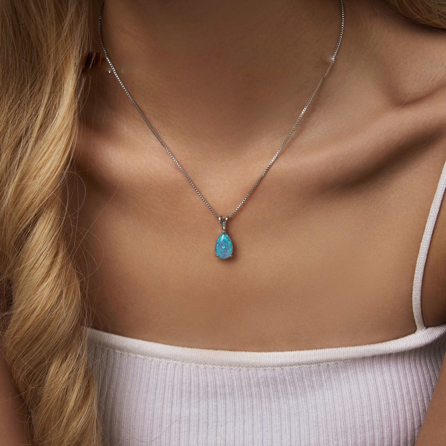 Frau mit silberner Halskette und blauem Opal-Anhänger, eleganter Schmuck, Nahaufnahme.