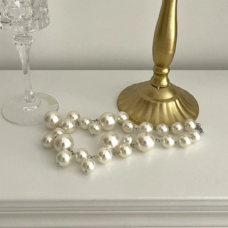 Perlenkette auf weißem Tisch neben goldener Lampe und Kristallglas, eleganter Schmuck.