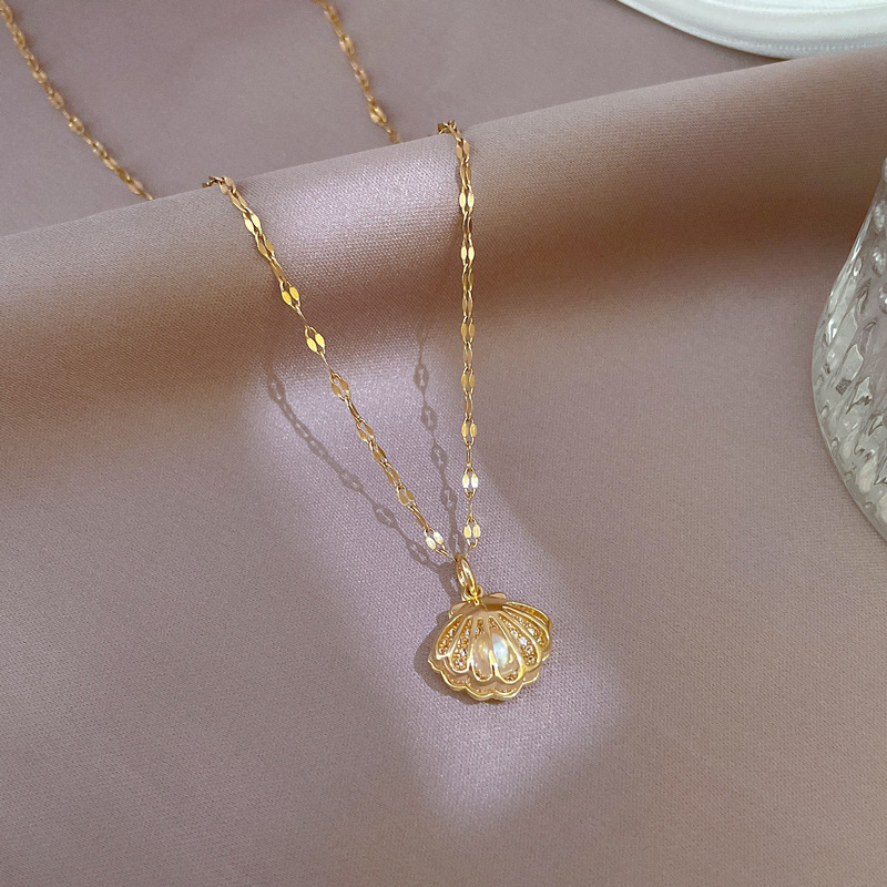 Goldene Muschelkette mit Perlenanhänger auf rosa Stoff, eleganter Schmuck für Damen.