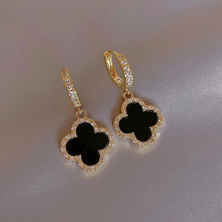 Goldene Ohrringe mit schwarzem Kleeblatt-Anhänger und Strasssteinen, eleganter Schmuck.