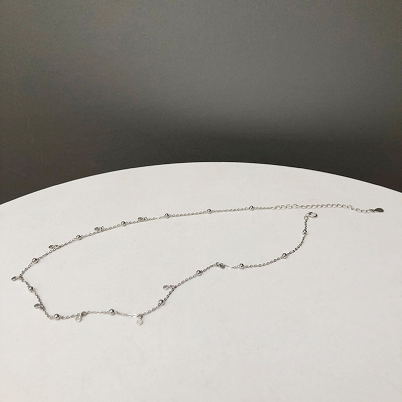 Silberne Halskette mit kleinen Anhängern auf weißem Tisch, minimalistisches Schmuckdesign.