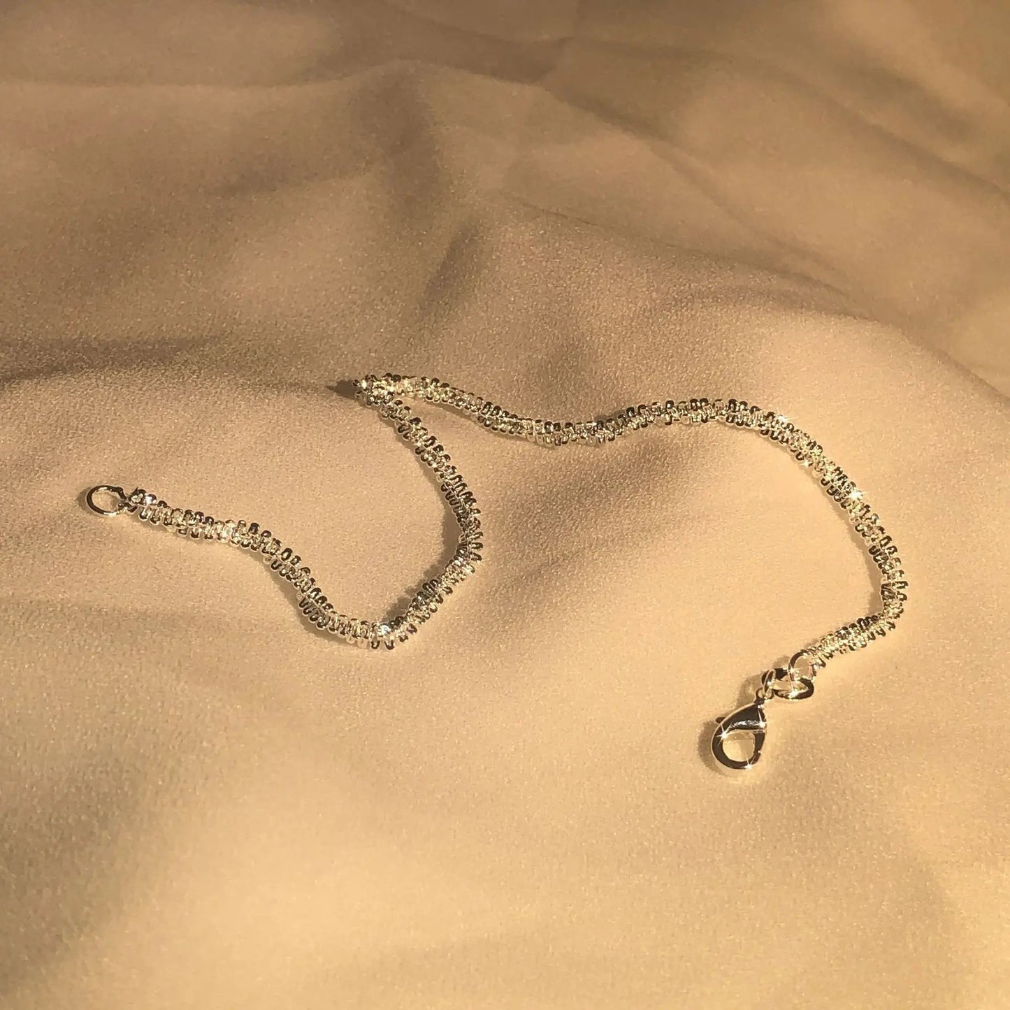 Silberne Halskette auf beigem Stoff, elegantes Schmuckdesign, Damenaccessoire.