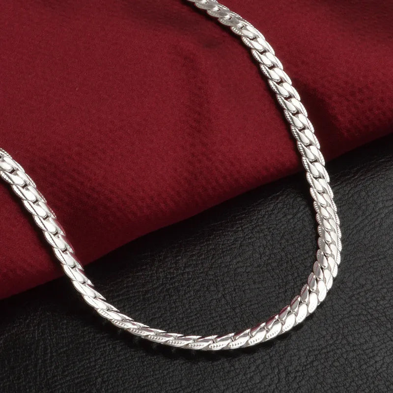 Silberne Halskette auf rotem Stoff, flach geflochten, elegantes Schmuckdesign, modisch.