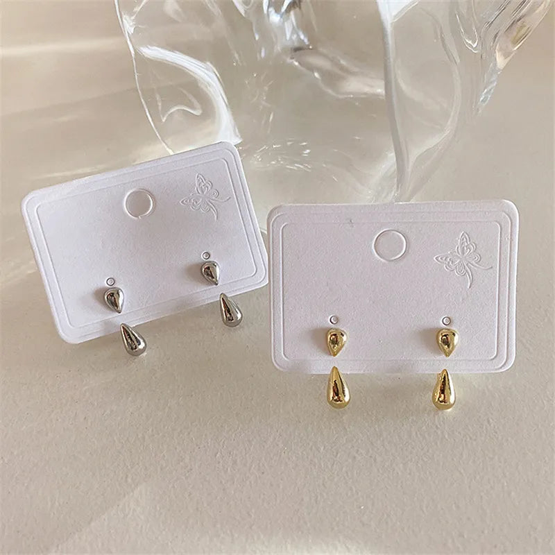 Zwei Paar Tropfen-Ohrringe, silber und gold, auf weißem Karton, elegantes Schmuckdesign.