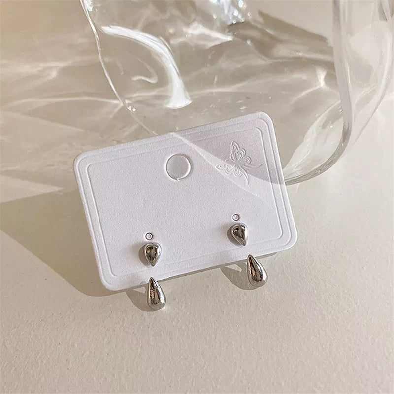 Silberne Tropfen-Ohrringe auf weißer Karte, minimalistisches Design, Schmuckaccessoire.