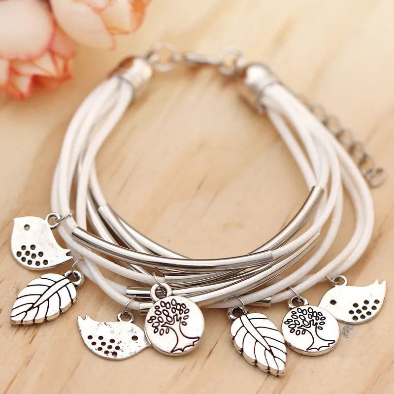 Mehrlagiges Armband mit weißen Bändern und silbernen Baum- und Blattanhängern.