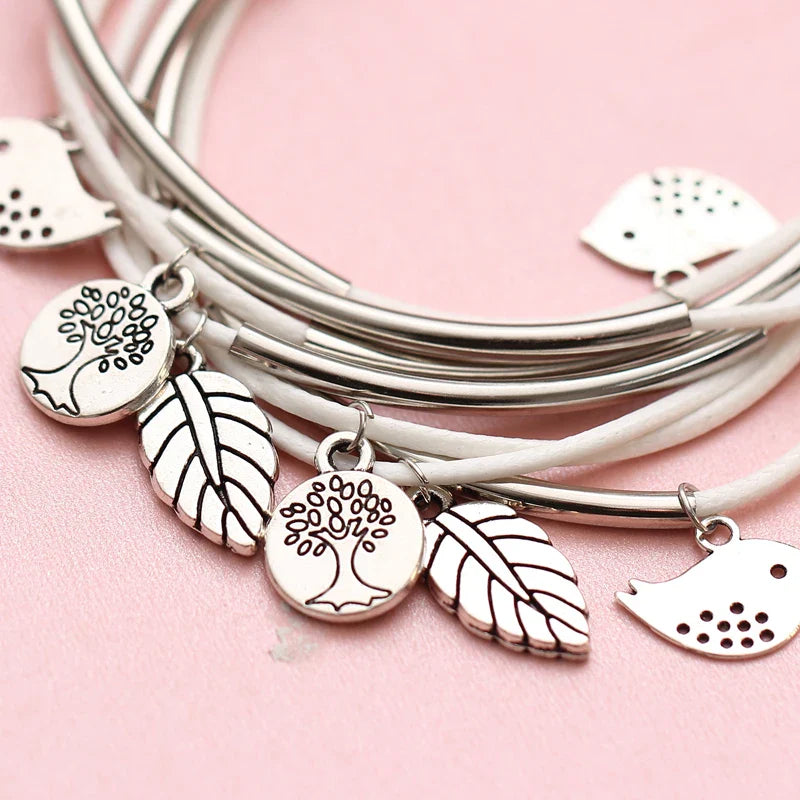 Silberne Armbänder mit Baum- und Blattanhängern auf rosa Hintergrund, Modeschmuck Accessoires.