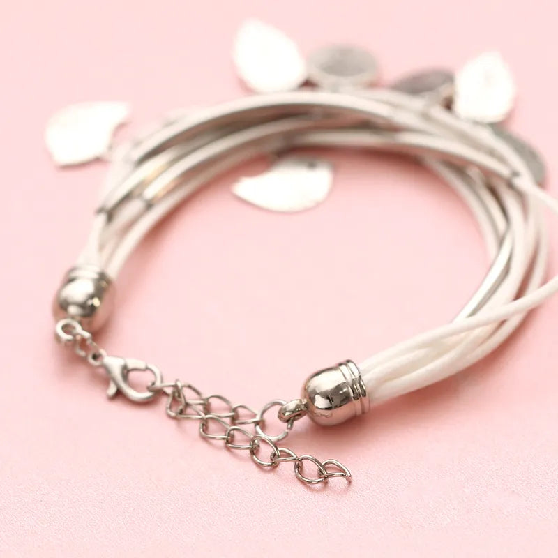 Mehrlagiges Armband aus weißem Leder mit silbernen Anhängern auf rosa Hintergrund.