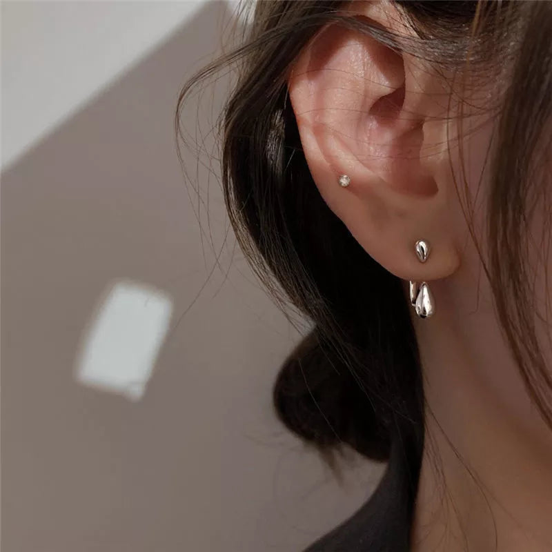 Frau mit silbernen Tropfen-Ohrringen und kleinem Ohrstecker, Nahaufnahme, eleganter Schmuck.