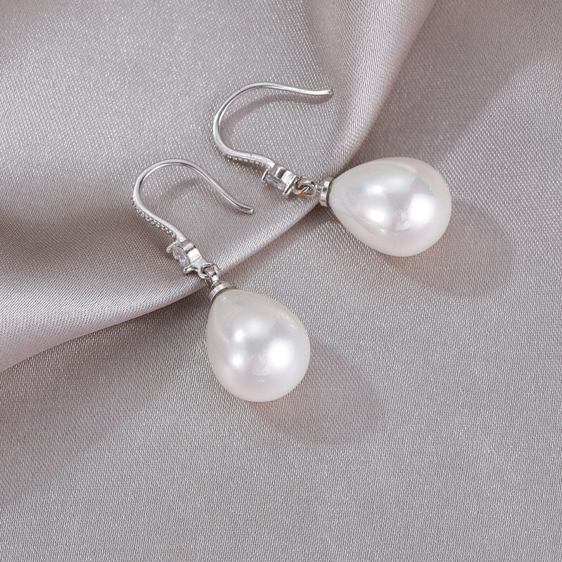 Silberne Ohrringe mit weißen Perlen, elegantes Schmuckdesign auf grauem Stoff.