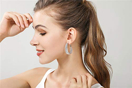 Frau mit silbernen Creolen, lächelnd, seitliches Profil, braunes Haar, weißes Oberteil.