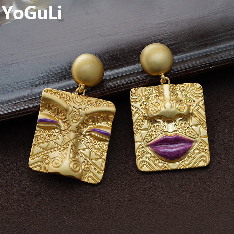 Asymmetrische goldene Ohrringe, Retro-Design, Messing, Gesichtsmotiv, lila Akzent.