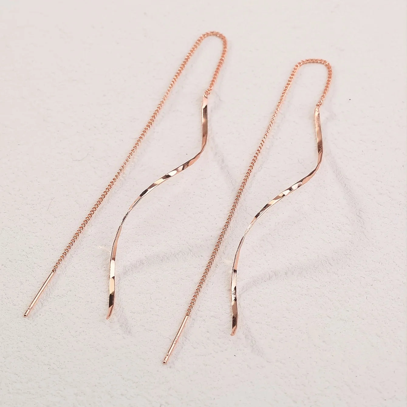 Roségoldene, lange Ohrringe mit geschwungenem Design, filigrane Kette, eleganter Schmuck.