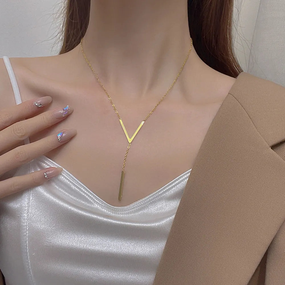 Frau mit goldener V-förmiger Halskette, elegantes Design, weißes Satin-Top, beige Blazer.