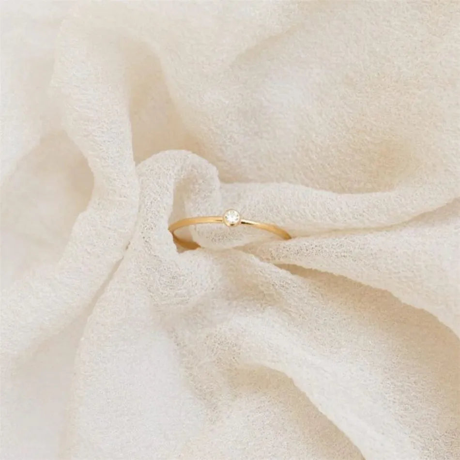 Goldener Ring mit Diamant auf cremefarbenem Stoff, eleganter Schmuck, minimalistisches Design.