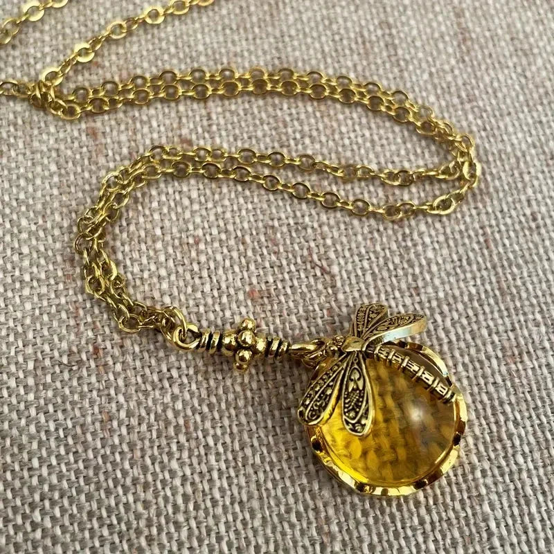 Goldene Halskette mit Libellenanhänger und gelbem Edelstein auf Leinenhintergrund.