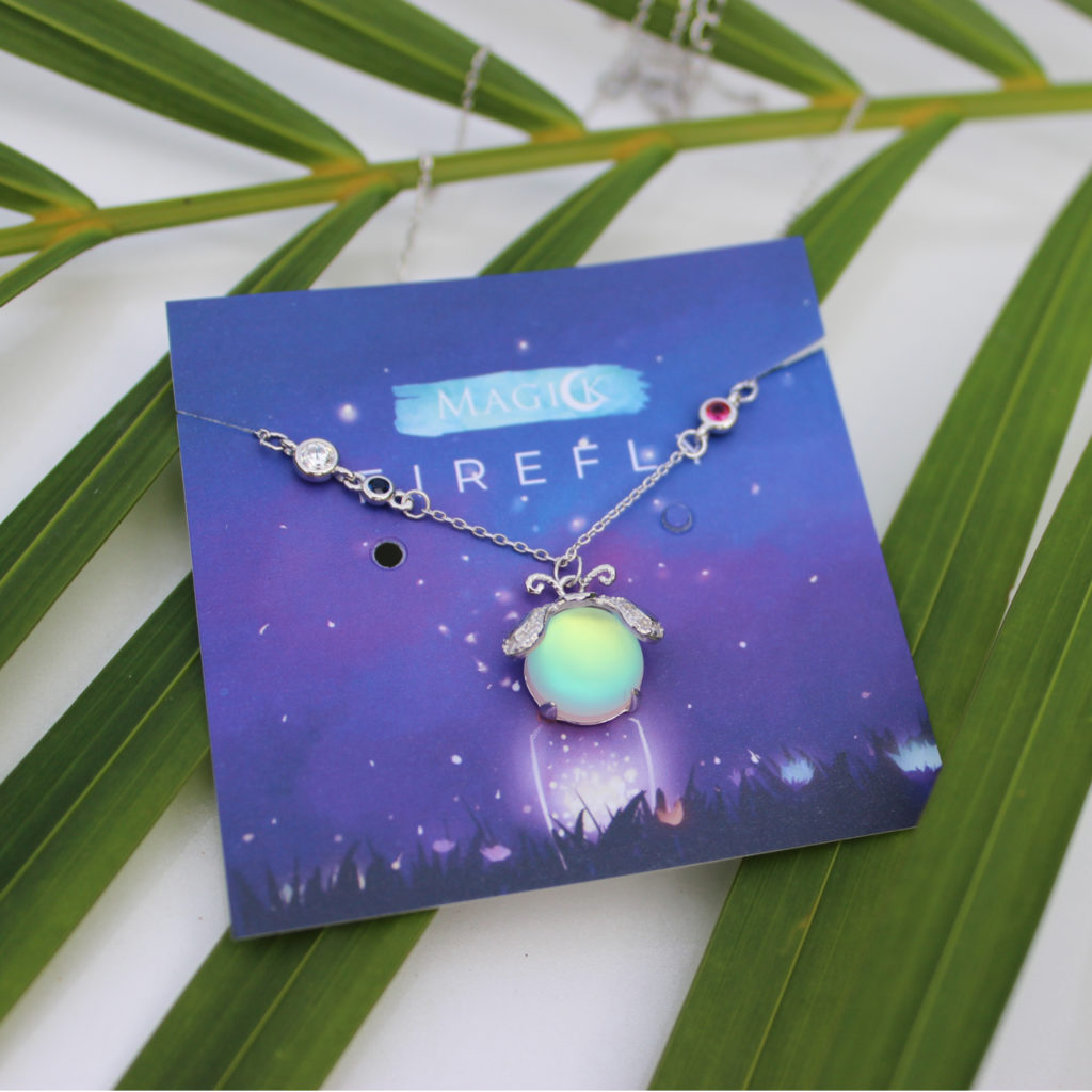 Leuchtkäfer-Halskette auf blauem Karton, silberne Kette, leuchtender Anhänger, Geschenkidee.