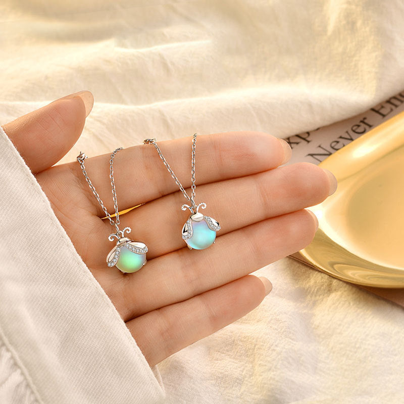 Zwei Glühwürmchen-Anhänger-Halsketten, silber, grün und blau, auf Hand liegend.