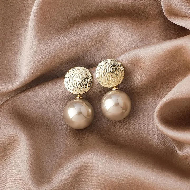 Goldene Ohrringe mit Perlen auf beigem Seidenstoff, eleganter Schmuck, modisches Accessoire.