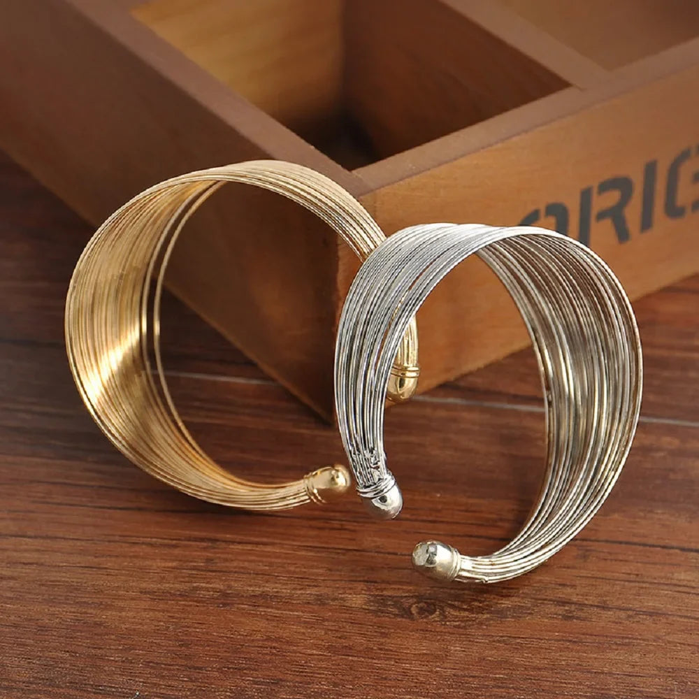 Zwei breite Armreifen aus Metall, gold und silber, auf Holztisch, modisches Schmuckdesign.