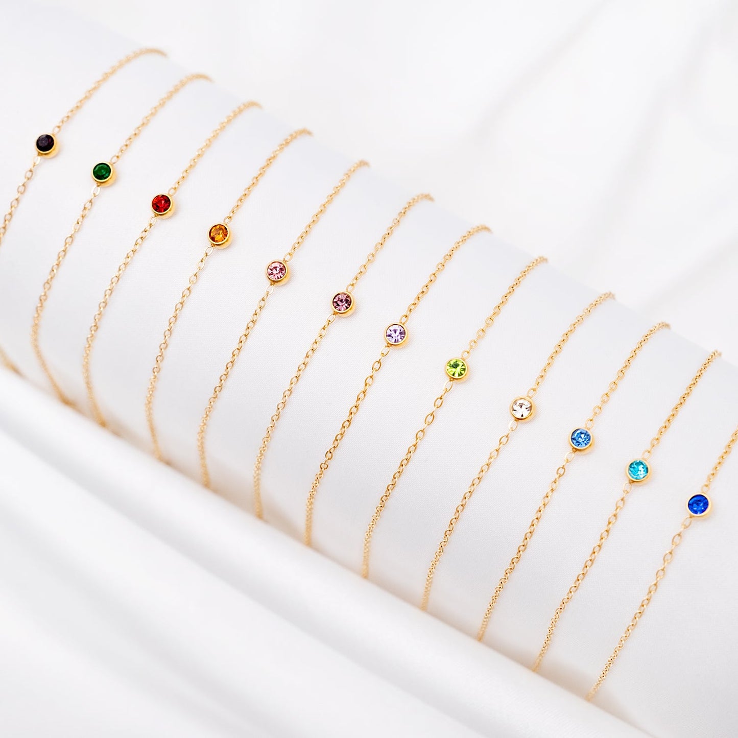 Goldene Geburtsstein-Armbänder auf weißem Hintergrund, verschiedene Farben, Schmuckaccessoires.