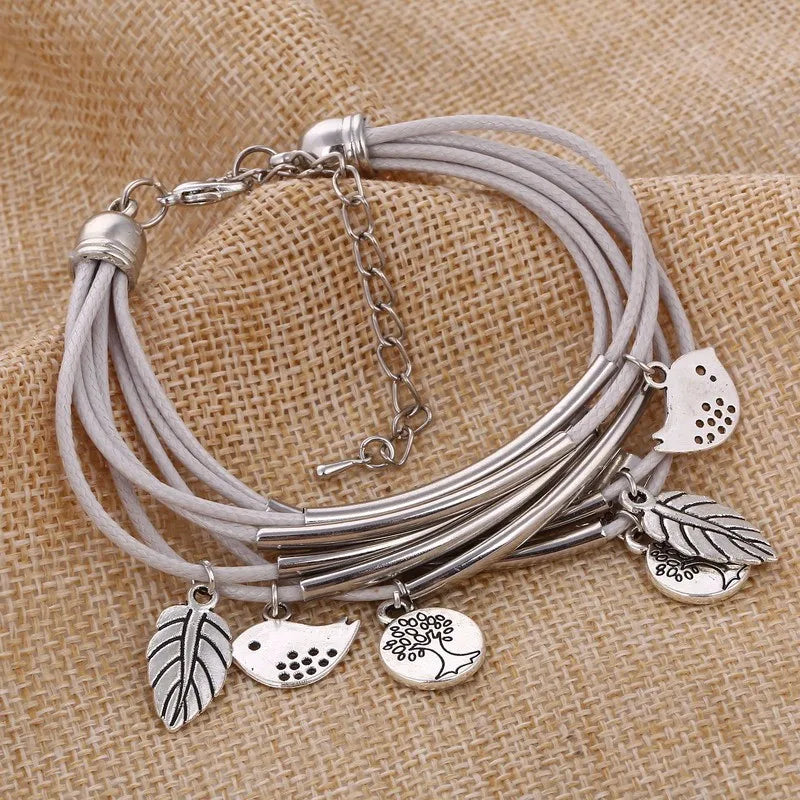 Graues Lederarmband mit silbernen Anhängern, Blätter und Vögel, auf Jutestoff.
