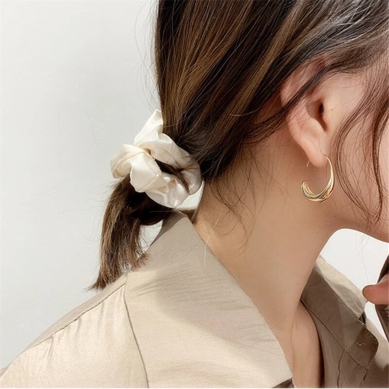 Frau mit beigem Haargummi und goldenen Ohrringen, eleganter Look, Modeaccessoires.