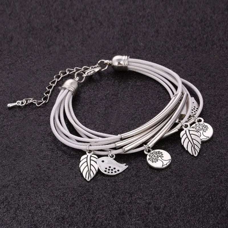 Mehrlagiges Armband aus Leder mit silbernen Baum- und Blattanhängern auf schwarzem Hintergrund.