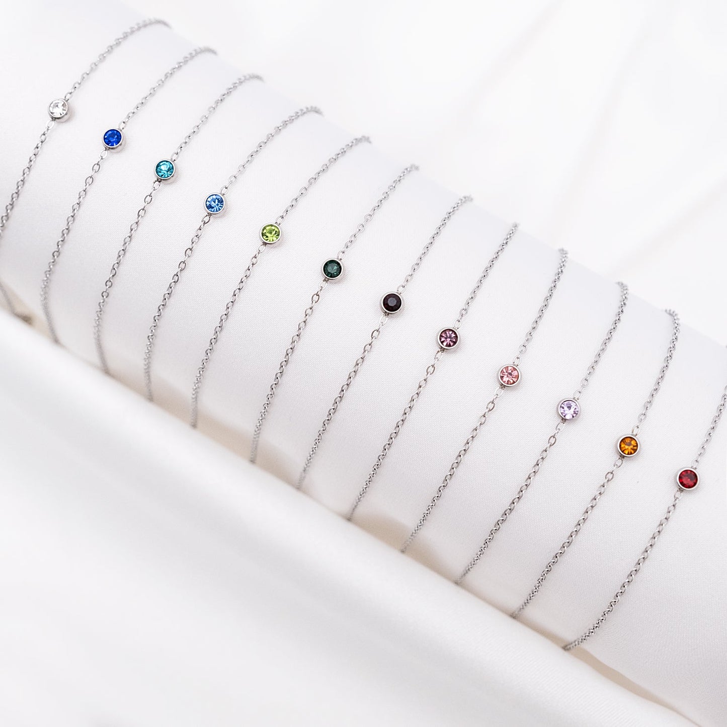 Silberne Geburtsstein-Armbänder auf weißem Hintergrund, verschiedene Farben, Schmuck für Damen.