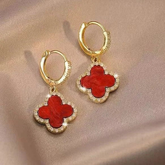 Goldene Ohrringe mit rotem Kleeblatt-Anhänger, funkelnde Steine, eleganter Schmuck.