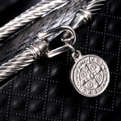 Silberarmband mit rundem Anhänger, geflochtenes Design, auf schwarzem Lederhintergrund.