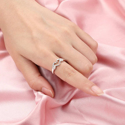 Silberner Ring mit geschwungenem Design auf Hand, rosa Seidenhintergrund.