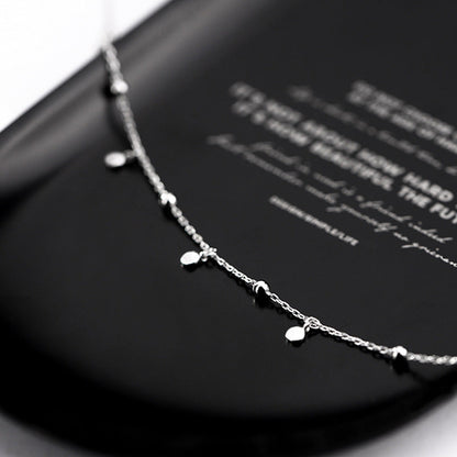 Silberne Halskette mit kleinen Anhängern auf schwarzem Hintergrund, eleganter Schmuck.