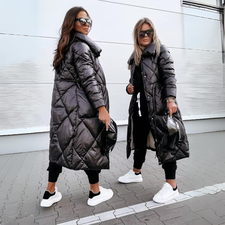 To kvinder side om side i sorte, ternet quiltede frakker, den ene set fra siden, begge med solbriller og hvide sneakers. 4