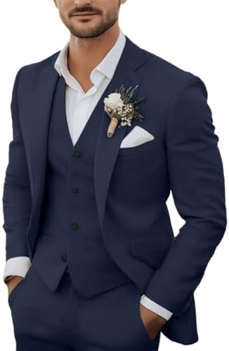 Mand i marineblå jakke og vest med hvid skjorte, blomsterbroche og hvidt lommetørklæde, hænderne i lommerne. 1