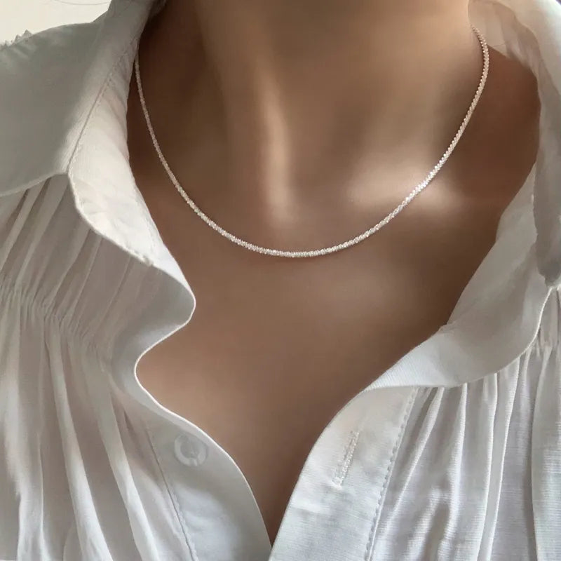 Weiße Perlenkette auf weißer Bluse, eleganter Schmuck für Damen, minimalistisches Design.