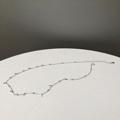 Silberne Halskette mit kleinen Anhängern auf weißem Tisch, minimalistisches Schmuckdesign.