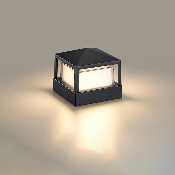Firkantet sort lampe med pyramideformet låg og varmt lys, set skråt fra siden på neutral baggrund. 10
