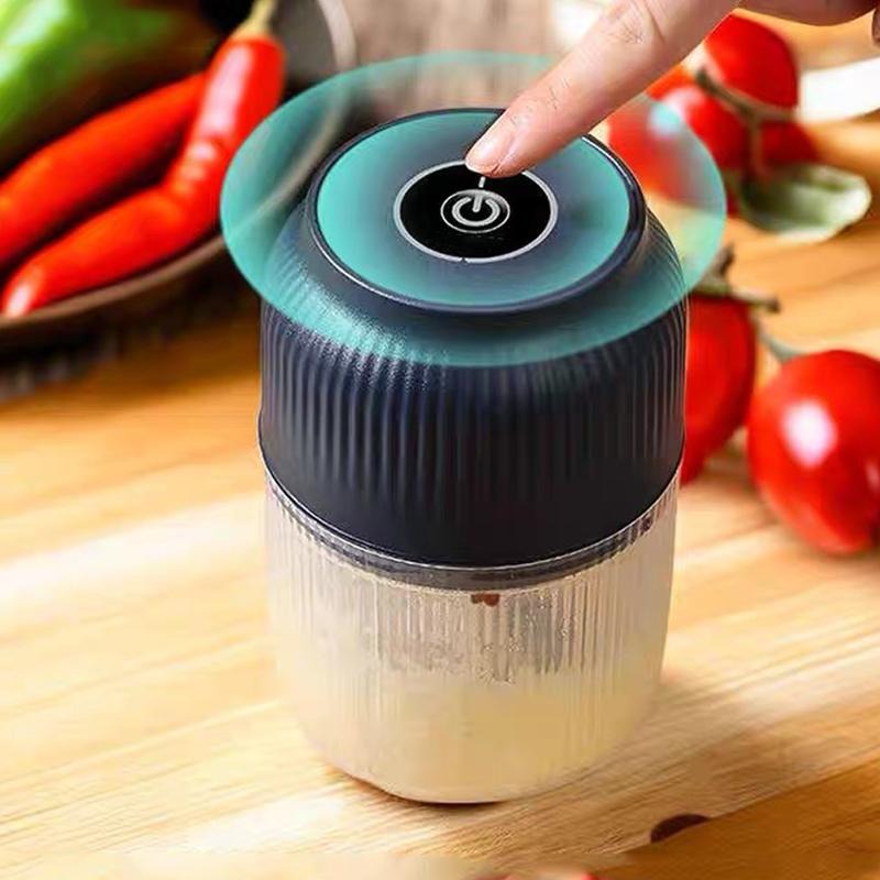 Et fingertryk på tænd-knappen øverst på den mørkeblå hakker, med røde chilier og tomater i baggrunden. 2