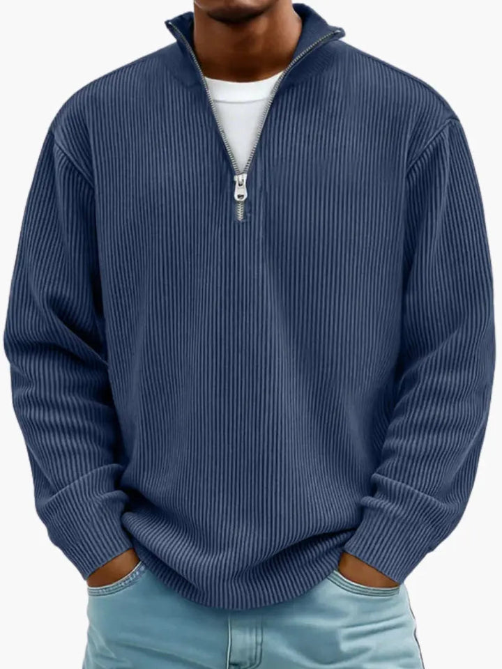Model i marineblå ribstrikket trøje med kvart lynlås og høj krave, hvid T-shirt under og lyseblå jeans. 5
