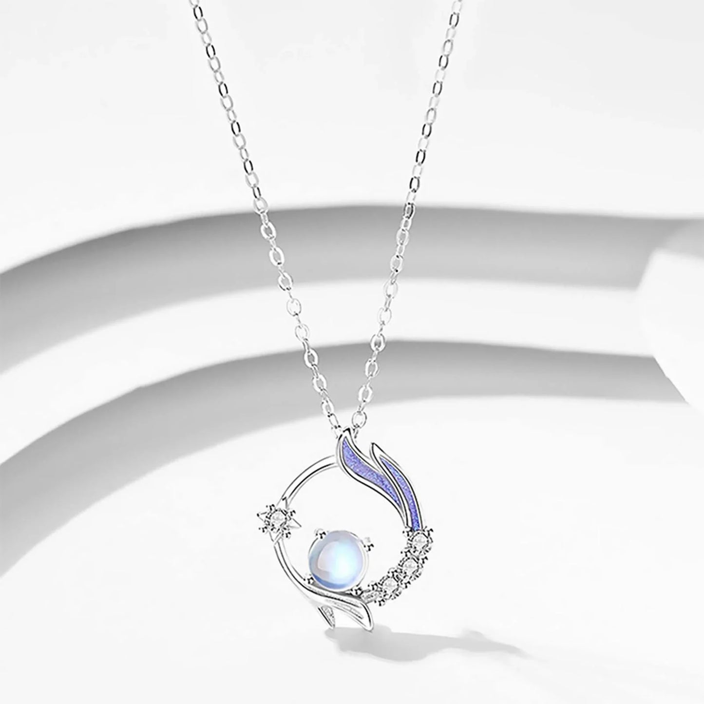 Silberne Halskette mit rundem Anhänger, blauer Perle und Kristallen, elegantes Schmuckdesign.