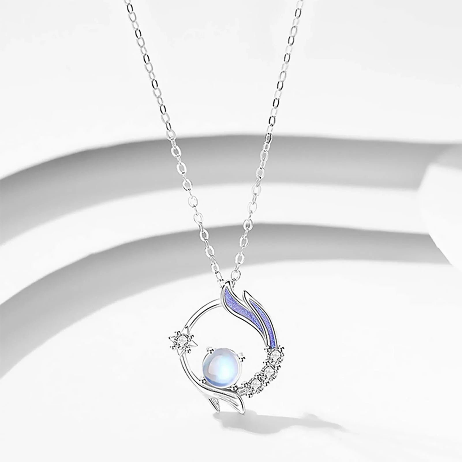 Silberne Halskette mit rundem Anhänger, blauer Perle und Kristallen, elegantes Schmuckdesign.