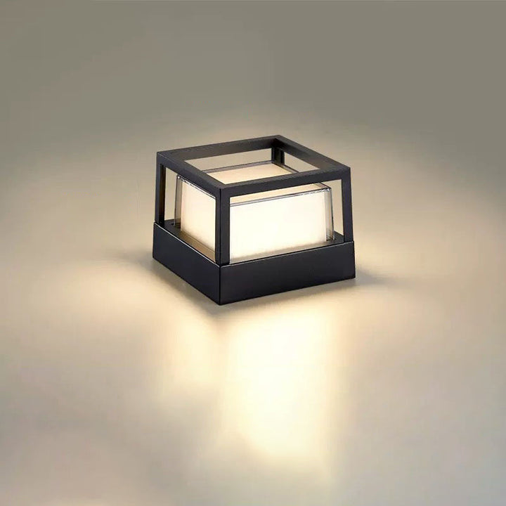 Firkantet sort lampe med åben kubeformet ramme og lysende skærm, set skråt på neutral baggrund. 11