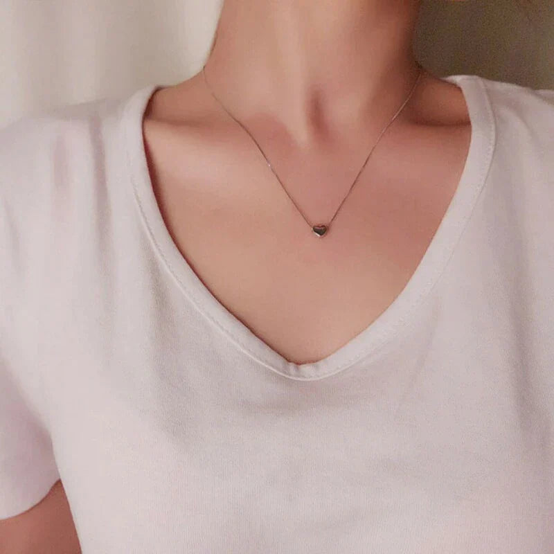 Frau mit Herzanhänger-Halskette, silber, V-Ausschnitt, weißes T-Shirt, eleganter Schmuck.