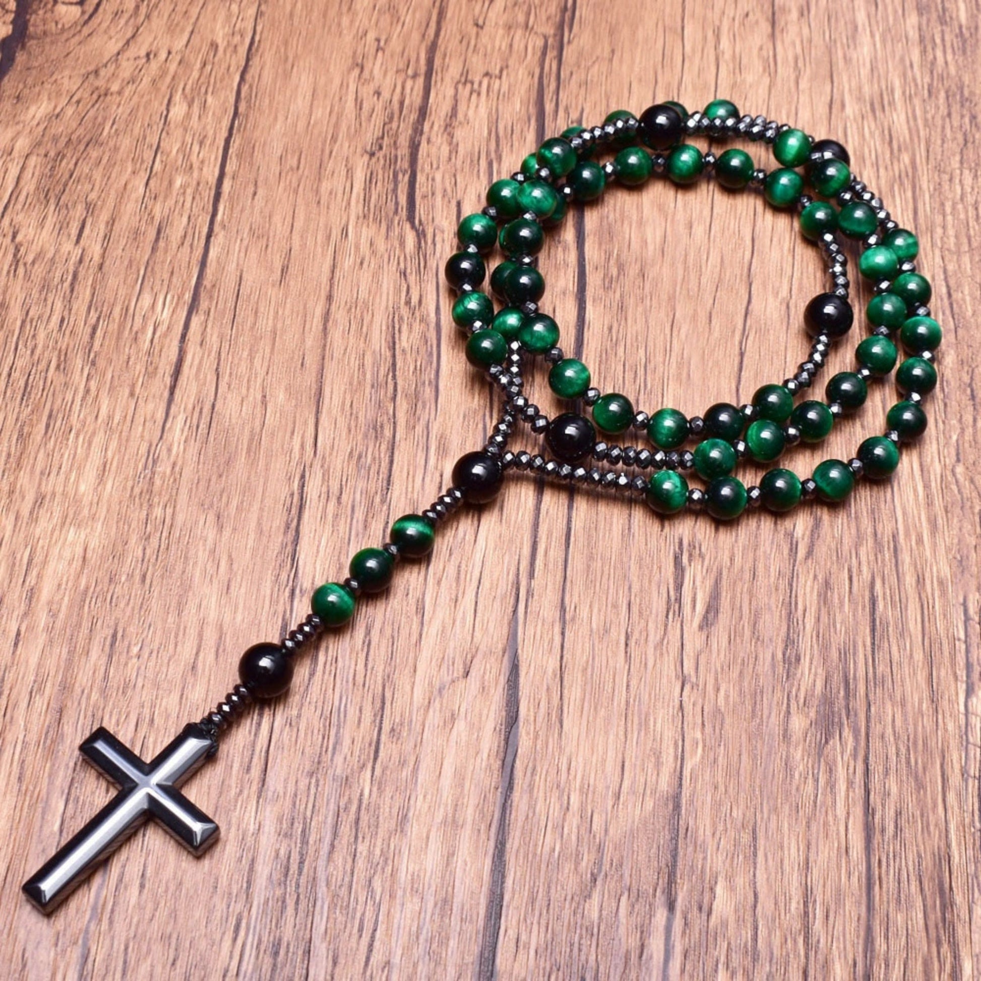 Grüner Rosenkranz mit schwarzen Perlen und Kreuz auf Holzhintergrund, religiöses Schmuckstück.