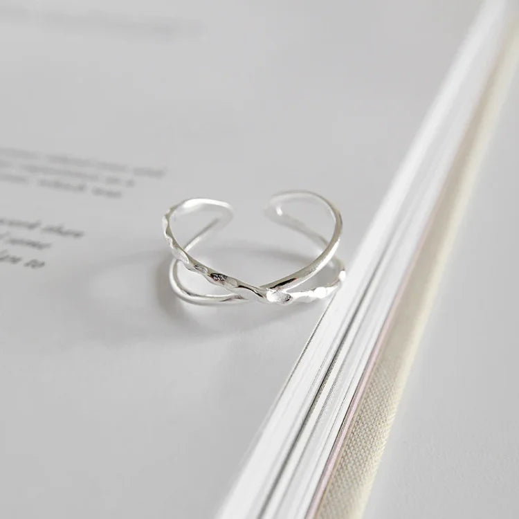 Silberner, verstellbarer Ring mit elegantem, gedrehtem Design auf weißem Hintergrund.