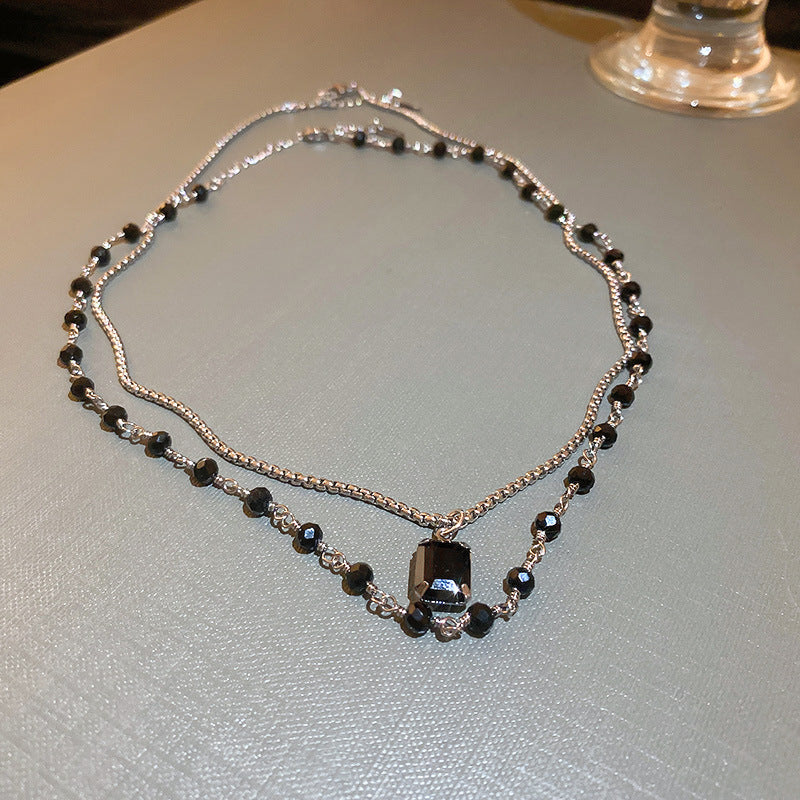 Silberne Halskette mit schwarzen Perlen, elegantes Schmuckdesign, auf grauem Hintergrund.