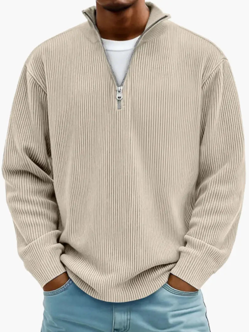 Model i sandfarvet beige ribstrikket trøje med kvart lynlås og høj krave, hvid T-shirt under og lyseblå jeans. 4
