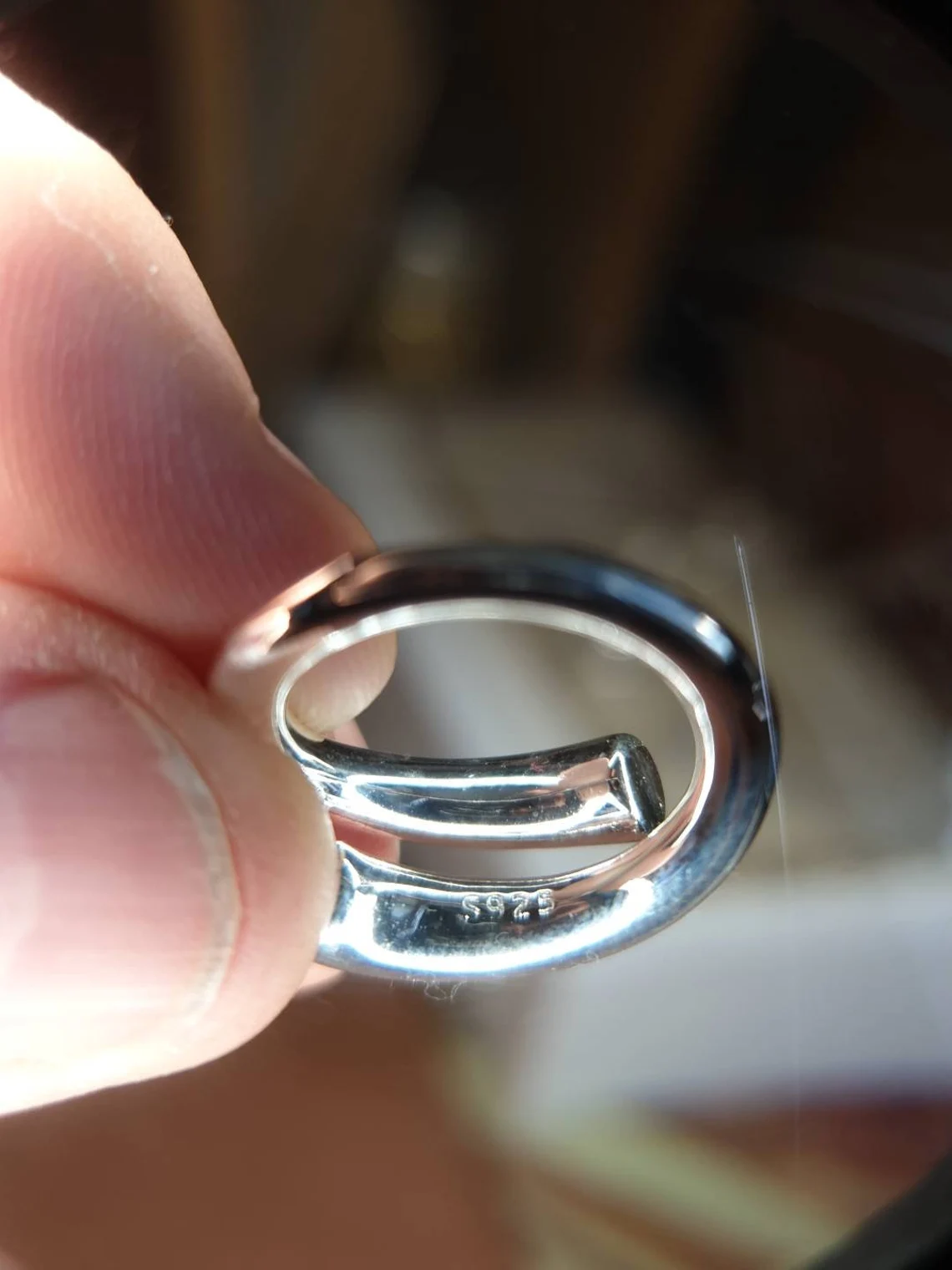 Silberner ovaler Schlüsselanhänger, glänzend, handgehalten, Nahaufnahme, Metallaccessoire.