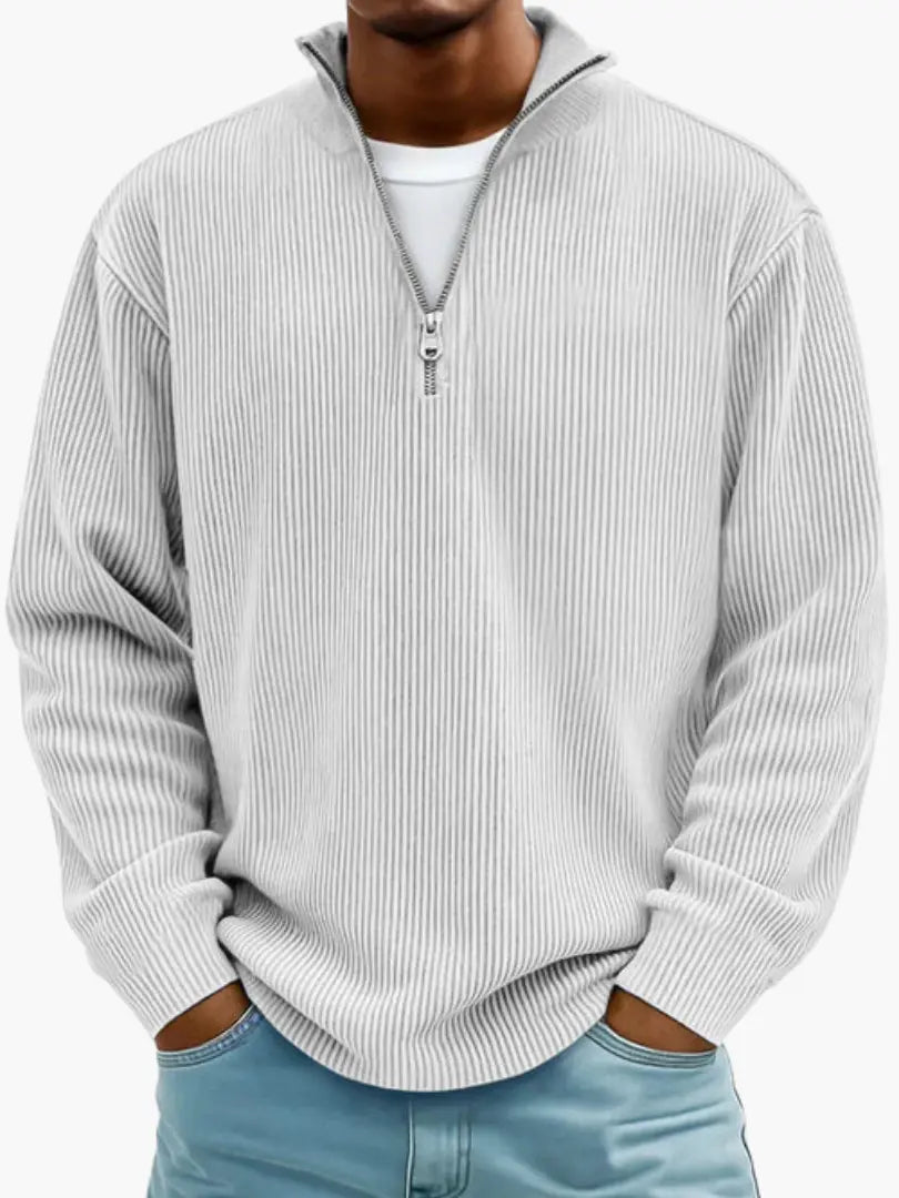 Model i lysegrå, næsten hvid ribstrikket trøje med kvart lynlås og høj krave, hvid T-shirt under og lyseblå jeans. 6